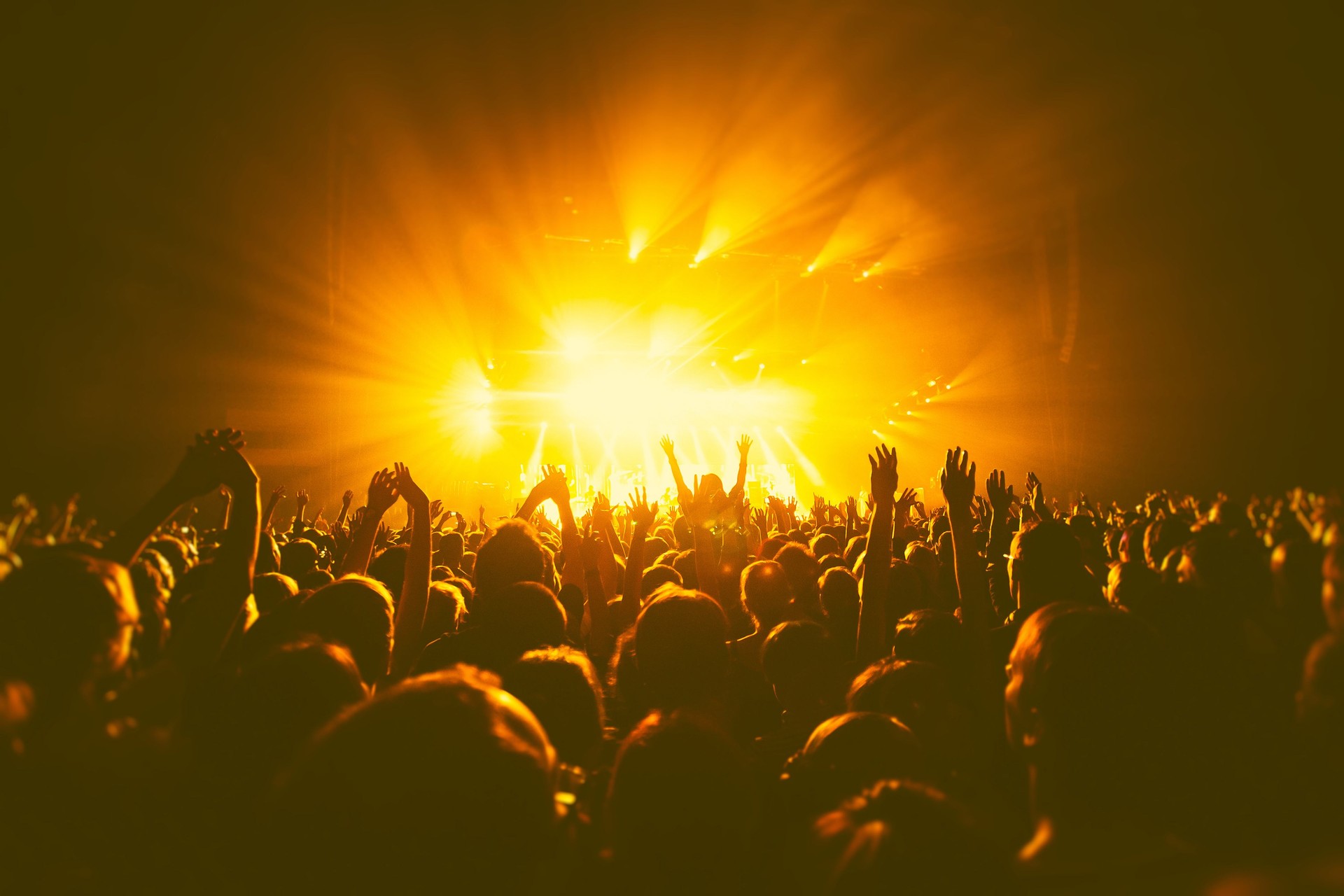 A crowded concert hall with scene stage orange and yellow lights, rock show performance, with people silhouette, colourful confetti explosion fired on dance floor air during a concert festival